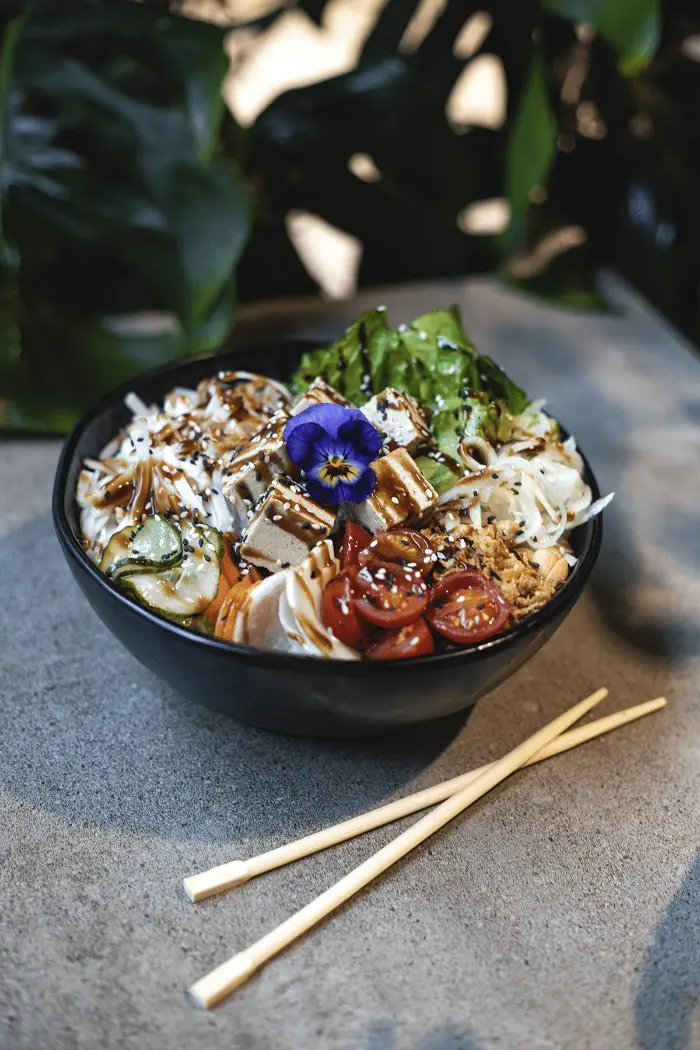 Bowl mit Reisnudeln, Tomaten, Gemüse und essbarer Blüte