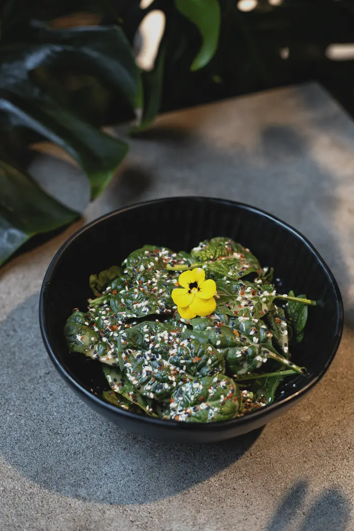 Schale mit grünem Salat, Sesam und essbarer Blüte